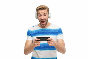 Kulaklıklı erkek oyuncu akıllı telefonuyla online video oyunu oynuyor. Beyazlar içinde izole edilmiş oyun için akıllı telefon kullanan bir adam. Akıllı telefondan oyun oyna. Oyun yaşam tarzı. Müzik ve oyun. Çevrimiçi kazanma.