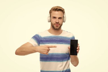 Beyazda izole edilmiş kablosuz kulaklıklı modern telefon. Milenyum adamı kulaklıkla müzik dinler. Telefon kullanan kulaklıklı bir adam. Z jenerasyonundaki adam telefon ekranı gösteriyor, kopyala uzayı. İşaret parmağı.