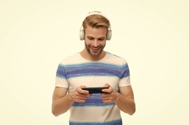 Beyazlar içinde izole edilmiş oyun için akıllı telefon kullanan bir adam. Akıllı telefondan oyun oyna. Oyun yaşam tarzı. Müzik ve oyun. Kulaklıklı erkek oyuncu akıllı telefon uygulaması ile çevrimiçi video oyunu oynuyor.