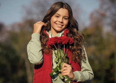 Genç kız gülüyor ve dışarıda bir buket çiçek var. Düşen buketi olan genç bir kızın fotoğrafı. Dışarıda güz çiçekli genç bir kız. Sonbahar çiçekli genç kız buketi.