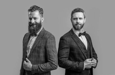 Pozitif smokinli iki adam. Stüdyoda resmi kıyafet giyen adamlar. Resmi takım elbiseli şık erkekler. Smokinli adamlar gri arka planda izole edilmiş..