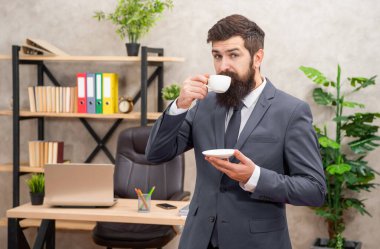 positive mature entrepreneur in jacket having coffee break at office, morning.