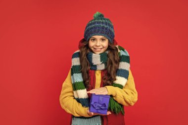 Kışın giyilen mutlu çocuk kırmızı arka planda bir kutu tutuyor, xmas.