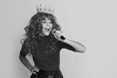 smiling child in crown with microphone on yellow background.