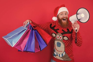 Sakallı adam elinde alışveriş torbalarıyla megafona bağırıyor. Noel Baba Noel indirimi duyurusu yapıyor. Tatil indirimi duyurusu. Dükkan duyurusu. Mutlu Noeller..