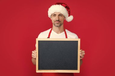 smiling mature man in new year hat and apron hold blackboard with copy space. clipart