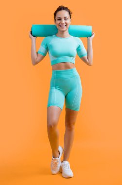 smiling woman in sportswear with fitness mat in studio. fitness woman in sportswear hold mat isolated on yellow background. fitness and sport.