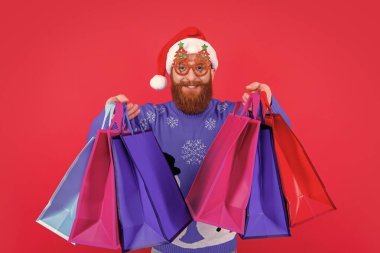 xmas shopping sale. positive man with shopping bag after xmas sale. santa man with xmas shopping bag at sale isolated on red. clipart