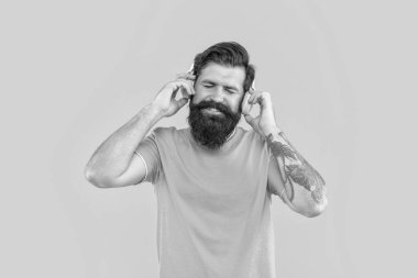 Gülümseyen havalı adam müzik dinler. Sakallı adam sarı arka planda izole edilmiş kulaklıkla müzik dinliyor. Adam kulaklıkla müzik dinliyor. Müzik konseptini dinle. Kulaklıklı adamın stüdyo fotoğrafı..