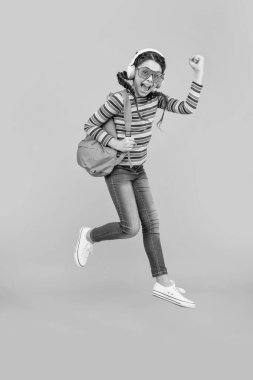 Kendinden geçmiş enerjik liseli kız atlıyor ve kazanan hareketi sarı arka planda yapıyor. Okul eğitimi. Okula geri dön..