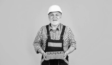 happy senior man bricklayer in hard hat on yellow background.