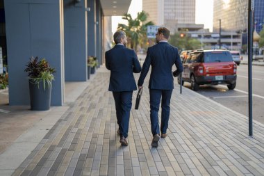 İki iş adamı ya da iş arkadaşı iş yerine giderken yolda yürürler ve konuşurlar..