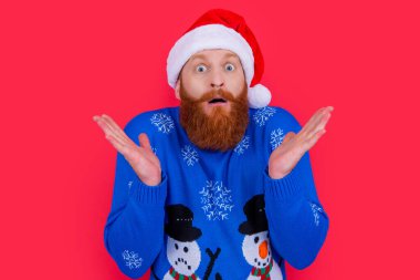 Yeni yıl süveteri ve kırmızı arka planda izole edilmiş Noel Baba şapkası giyen beyaz bir adam. Yılbaşı partisindeki adam. Mutlu yıllar..