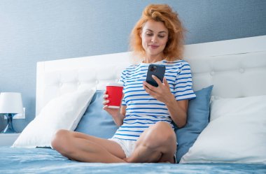 Telefonda internette kahve sörfü yapan neşeli bir kadın. Evde telefonuyla internette sörf yapan bir kadın. Kadının evinde internet sörfü.