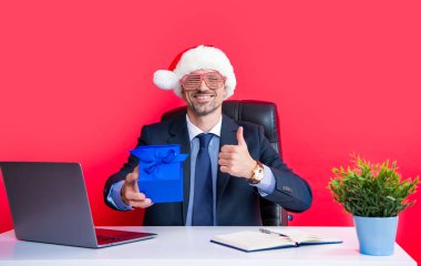Olgun adam kırmızı Noel Baba şapkası takıyor ve parti gözlükleri hediye kutusunu tutuyor. başparmak yukarı.