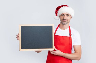 Noel Baba şapkalı ve önlüklü neşeli olgun adam fotokopi alanı olan karatahtayı tut..