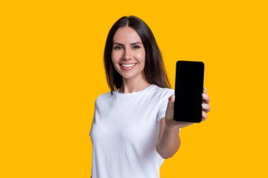 Sarıda izole edilmiş bir telefon gösteren genç kız. Milenyum kadını. Yeni telefon uygulaması. Kız reklam veriyor. Ürünü sunuyorum. İş uygulamasının reklamı. Telefon ekranı sunan bir kadın. Seçici odak.