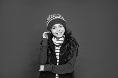 Kalın giysiler giyen çocuk portresi. Olumlu duygularını ifade et. Kış modası. Şapkalı, kıvırcık saçlı, gülümseyen çocuk. Kırmızı arka plandaki genç kız..