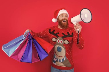 Sakallı adam elinde alışveriş torbalarıyla hoparlöre bağırıyor. Noel Baba indirim duyurusu yapıyor. Noel indirimi duyurusu. Dükkan duyurusu. Mutlu Noeller..