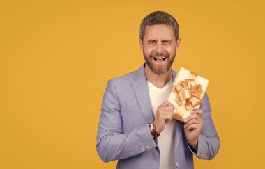 photo of surprised guy holding occasion gift box. guy hold gift box isolated on yellow background. guy hold gift box in studio. guy with gift box for holiday.