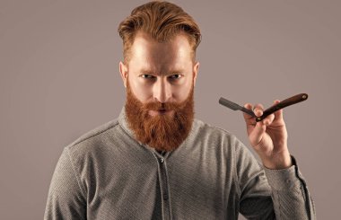 Berber stüdyosundaki yakışıklı adam. Adam tıraş olmak için berber bıçağını tutuyor. Gri arka planda berber bıçağıyla tıraş olan bir adam. Berber adam bıçakla tıraş oluyor..