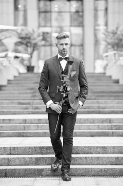 Smokinli şık bir adam. Smokin giymiş papyonlu bir adam dışarıda yürüyor. Kırmızı güllü yakışıklı smokinli adam..