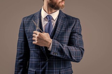 Berber makaslı sakallı adamın fotoğrafı, kopyalama alanı. Berber adam gri arka planda izole edilmiş bir makas tutuyor. Makasla berber adam. Berber stüdyosunda makaslı bir adam..