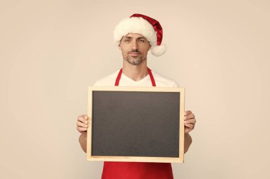 mature man smile in santa hat and apron hold blackboard with copy space. clipart