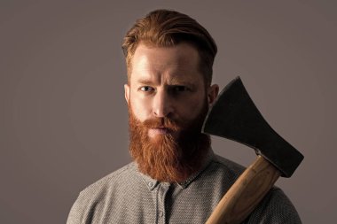 Keskin baltalı sakallı berber adamın kızıl sakalı var. Stüdyodaki sakallı berber. Berber konsepti. Kızıl sakallı sakallı sakallı adam gri baltayı soyutladı..