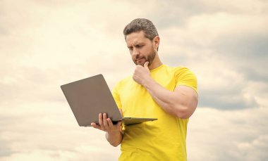 Düşünen adam gökyüzü arka planında dizüstü bilgisayarda çalışıyor..