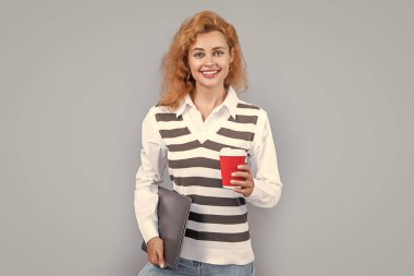 Stüdyoda serbest çalışan mutlu bir kadın. Dizüstü bilgisayarı ve kahvesi olan serbest bir kadın. Bilgisayarı tutan serbest çalışan bir kadın. Gri arka planda kahvesi olan bağımsız bir kadın..