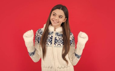 cheerful teen girl in warm winter knitted mittens and sweater in studio. teen winter girl isolated on red background. warm winter knitwear fashion. clipart