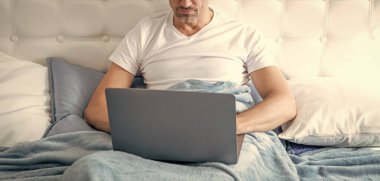 Gözlüklü olgun bir adam laptopla yatakta çalışıyor..