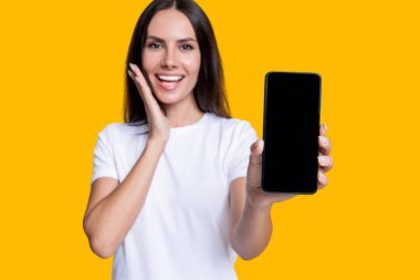 Kız reklam veriyor. Ürünü sunuyorum. İş uygulamasının reklamı. Telefon ekranı sunan bir kadın. Sarıda izole edilmiş bir telefon gösteren genç kız. Milenyum kadını. Yeni telefon uygulaması. En iyi teklif.