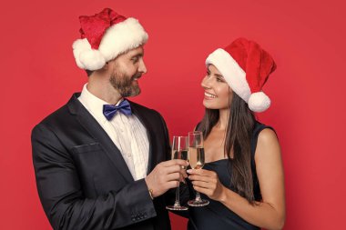 Stüdyodaki neşeli çifte mutlu Noeller. Çift Noel 'i kutluyor. Tatili kutlayalım. Xmas çifti kırmızı arka planda izole edilmiş şampanyayla kutluyor. Yılbaşı partisini çiftlerle kutlarız..