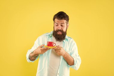 Sakallı, sarı arka planda kahve fincanı tutan yetişkin bir hippi..