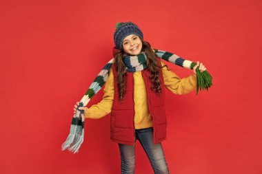 Kış şapkalı mutlu çocuk kırmızı arka planda eşarp tutuyor, sezon modası..