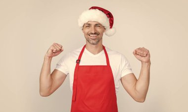 Kırmızı şef önlüğü ve Noel Baba şapkası takan mutlu olgun bir adam..