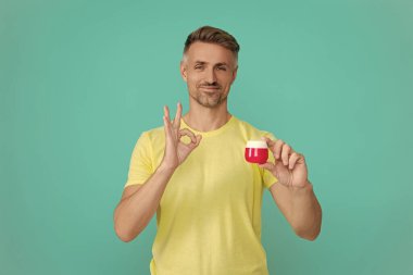 Erkek kozmetik ürünü sunan adam. Mavi renkte yüz kremi gösteren bir adam var. Olgun adam cilt kremi kullanır. Günlük alışkanlık ve kişisel bakım. Cilt güzelliği. Erkek güzellik kozmetiği. Tamam..