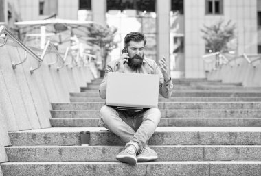 Merdivenlerde oturan mutsuz bir adam cep telefonuyla konuşuyor. Üzgün adam dışarıda dizüstü bilgisayarla arama yapıyor. Mobil iletişim. Telefon görüşmesi. Cep telefonu çağrısı.