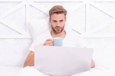 Adam yatakta yatıp dizüstü bilgisayarla internette sörf yapıyor. Bilgisayarda evden çalış. Hafta sonu işkolik. Sabah kahvesi hazır. Yatakta serbest çalışan. Milenyum adamı evde dizüstü bilgisayarda çalışıyor..