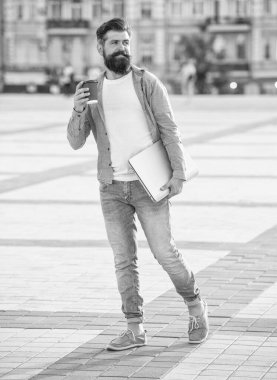 Sabahları kahve içen mutlu adam. Sakallı adam elinde yemek fincanı ve laptop tutuyor. Açık havada modaya uygun bir adam. Caddede gülümseyen beyaz adam..