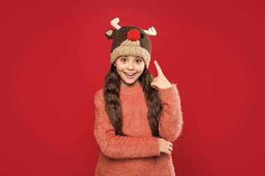 idea of teen child in winter fashion hat isolated on red. teen child wear sweater and winter fashion hat in studio. winter fashion for teen child. teen child fashion model in winter earflap hat. clipart