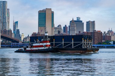 Römorkör Brooklyn köprüsünde mavna itiyor. Hudson Nehri, New York 'ta bir mavna ve römorkör. Manhattan şehir manzarası. New York 'taki gökdelenden harika bir manzara. Manhattan 'a doğru.