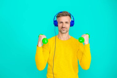 Olgun bir adam mavi üzerine izole edilmiş spor eğitimi yapar. Dambılı bir sporcu. Müzikli spor salonu. Spor salonu. Atletik egzersiz için müzik. Güçlü sporcu adam seni. Sportmenlik.