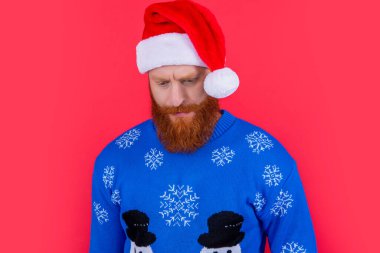 Kırmızı üzerine izole edilmiş ciddi bir Noel Baba portresi. Duygusuz suratlı, Noel Baba şapkası giyen sakallı adam. Noel partisi. Yılbaşı arifesi kutlaması. Kış tatili.