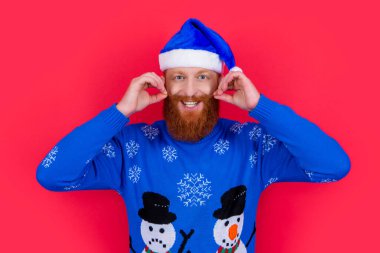 Noel Baba 'daki sakallı adam bükülmüş bıyık stüdyosu giyer. Kırmızı renkte izole edilmiş mutlu Noel Baba bıyığı çeviriyor. Noel partisine hazırlanıyorum. Noel kutlaması. Mutlu noeller. Mutlu yıllar..