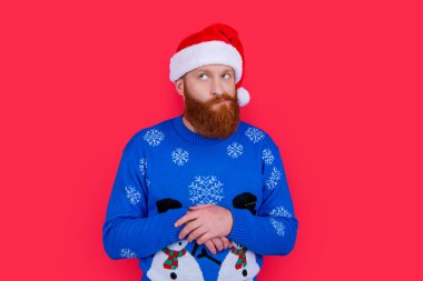 Kafkasyalı, yeni yıl süveteri ve Noel Baba şapkası giymiş kırmızı arka planda izole edilmiş bir adamı merak ediyordu. Yılbaşı partisindeki adam. Mutlu yıllar..