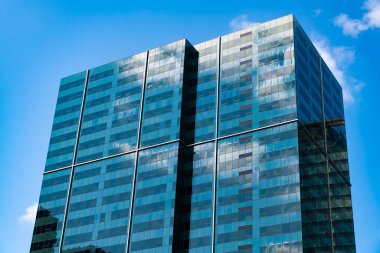 Şehir merkezinde gökdelenli. İş bölgesindeki ofis binası. Gökdelen mimarisi. Camdan yapılmış bir gökdelen. Modern cam bina. Şehir merkezindeki gökdelen. Yükseklik.