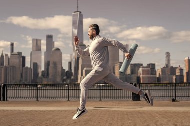 Spor takım elbiseli bir adam dışarıda spor yapmak için spor minderiyle Manhattan 'da koşuyor..